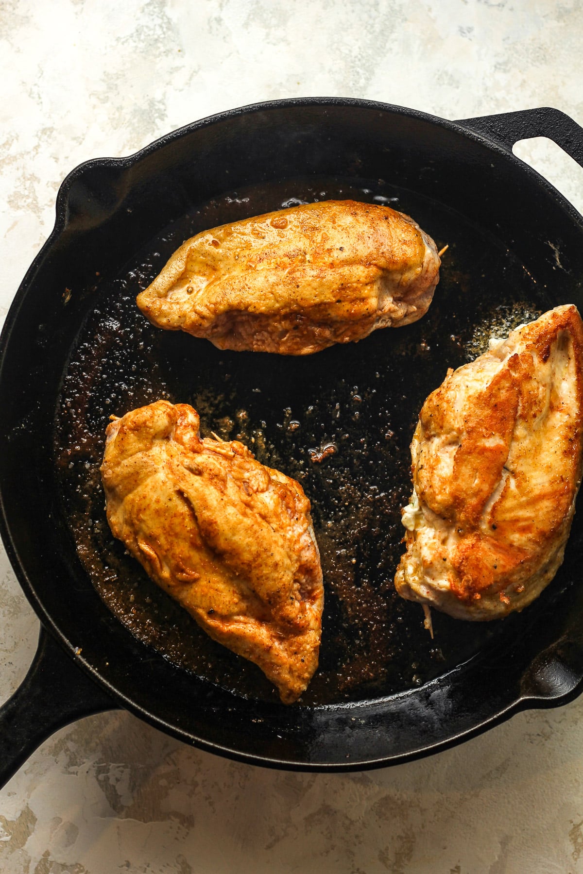 A skillet with three seared chicken breasts.