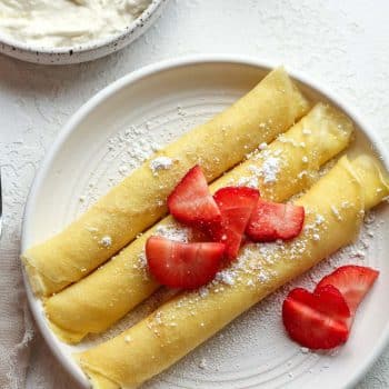 A plate of three rolled crepes stuffed with cream cheese filling.