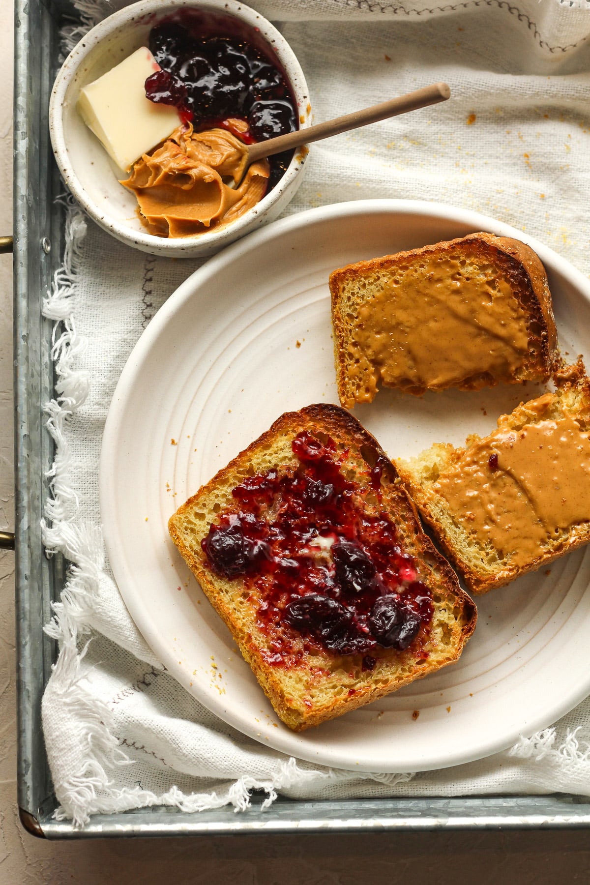 A tray with a plate with two pieces of English muffin bread topped with peanut butter and jelly.