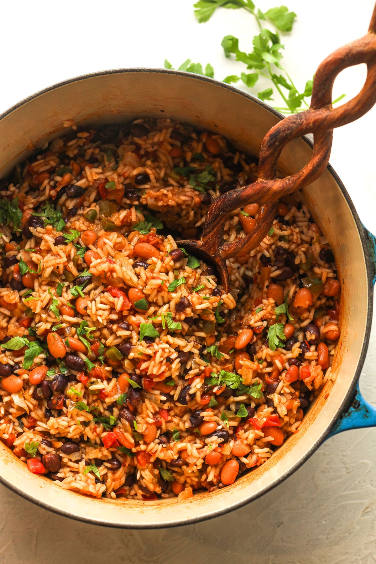 Overhead view of a stock pot of Mexican rice and beans with a wooden spoon.