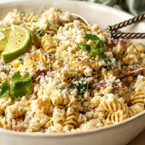 Side view of a bowl of street corn pasta salad with silver serving spoons.