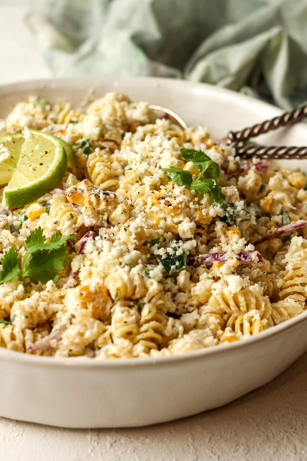 Side view of a bowl of street corn pasta salad with silver serving spoons.