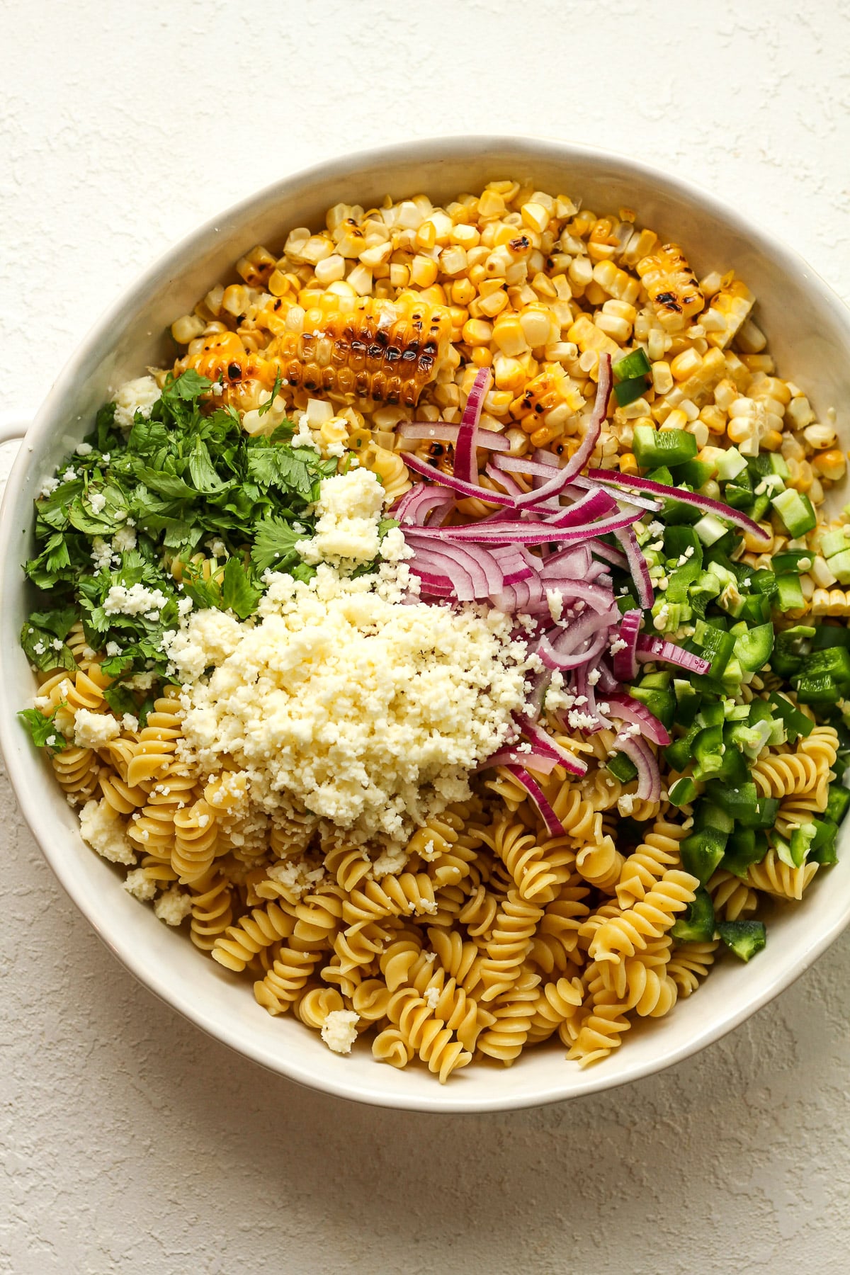 A bowl of the street corn pasta salad separated by ingredient.