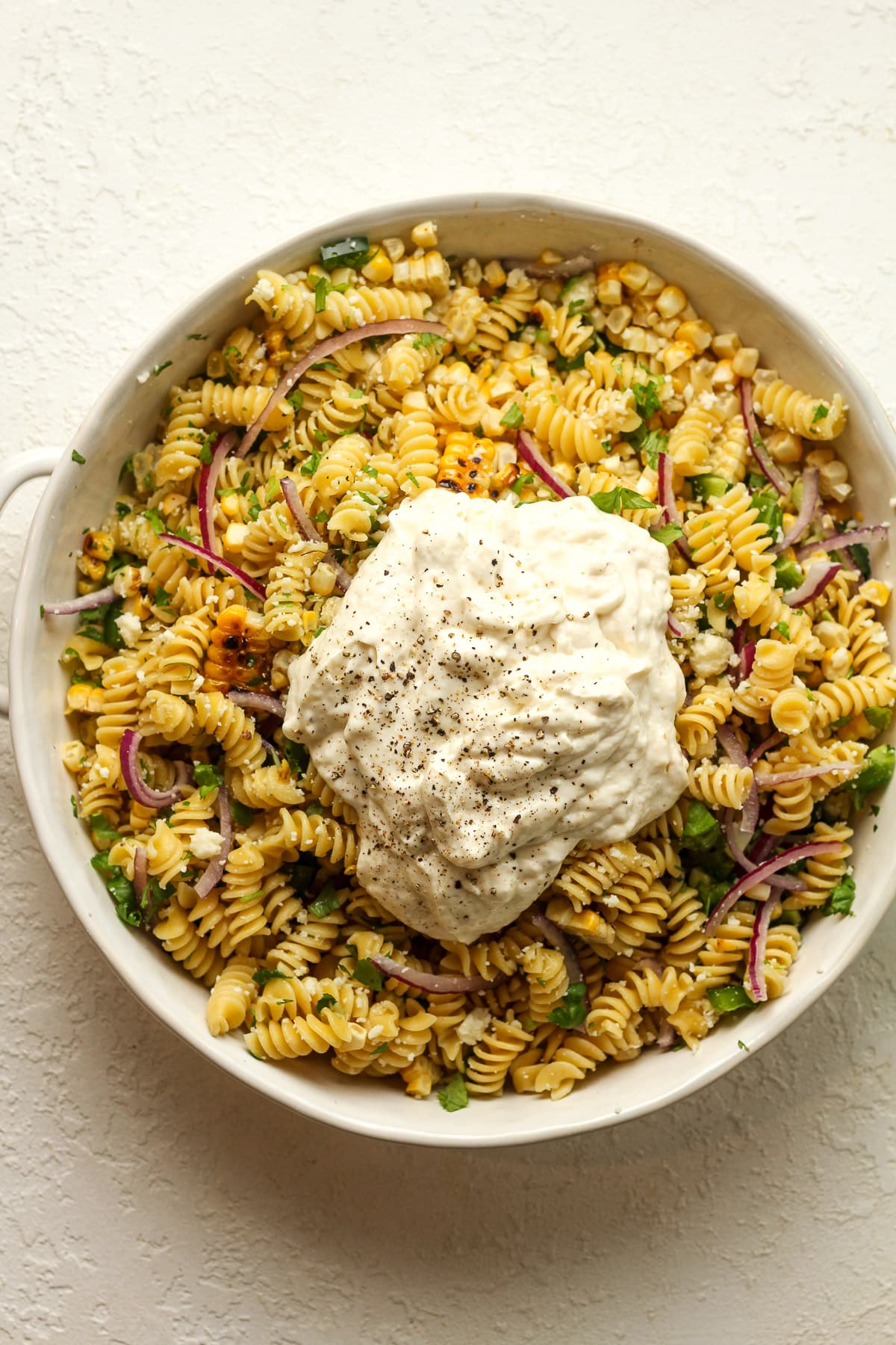 A bowl of the street corn pasta salad ingredients with the dressing on top.