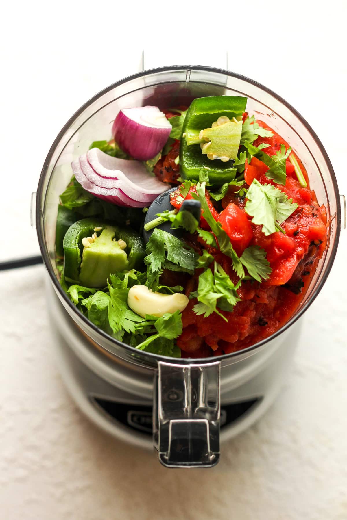 Overhead view of a food processor filled with the salsa ingredients before blending.