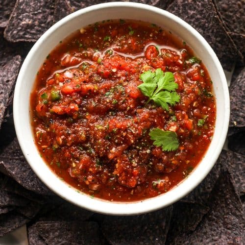 Overhead view of a bowl of blender salsa on a plate of blue corn chips.