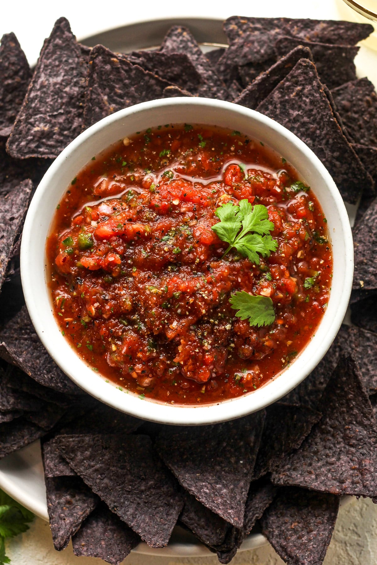 Overhead view of a bowl of blender salsa on a plate of blue corn chips.