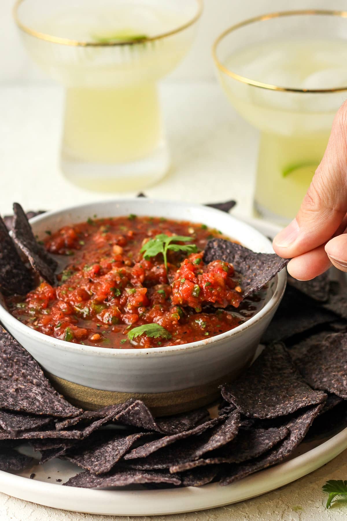 Closeup on a bowl of blender salsa and a hand dipping a blue chip.