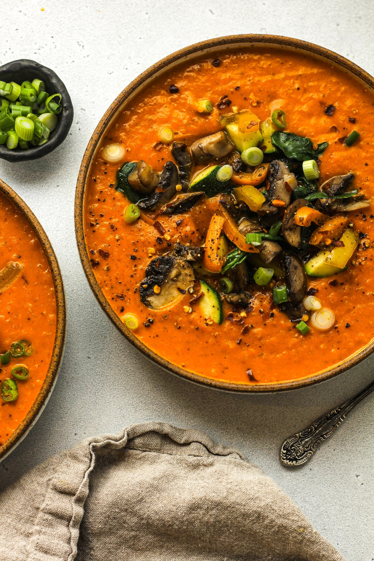 Overhead view of two bowls of coconut curry soup with sautéed veggies on top.