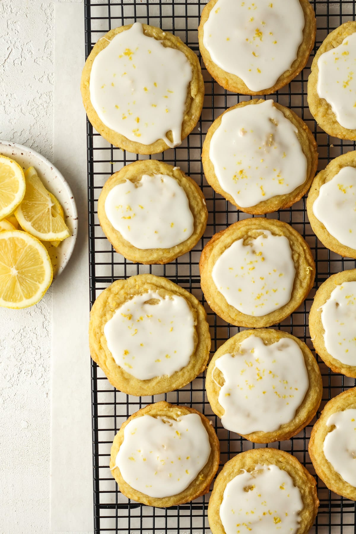 The lemon sugar cookies on a cooling rack next to a small plate of lemon slices.