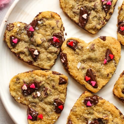 Overhead view of a plate of cookies cut into heart shapes with sprinkles.