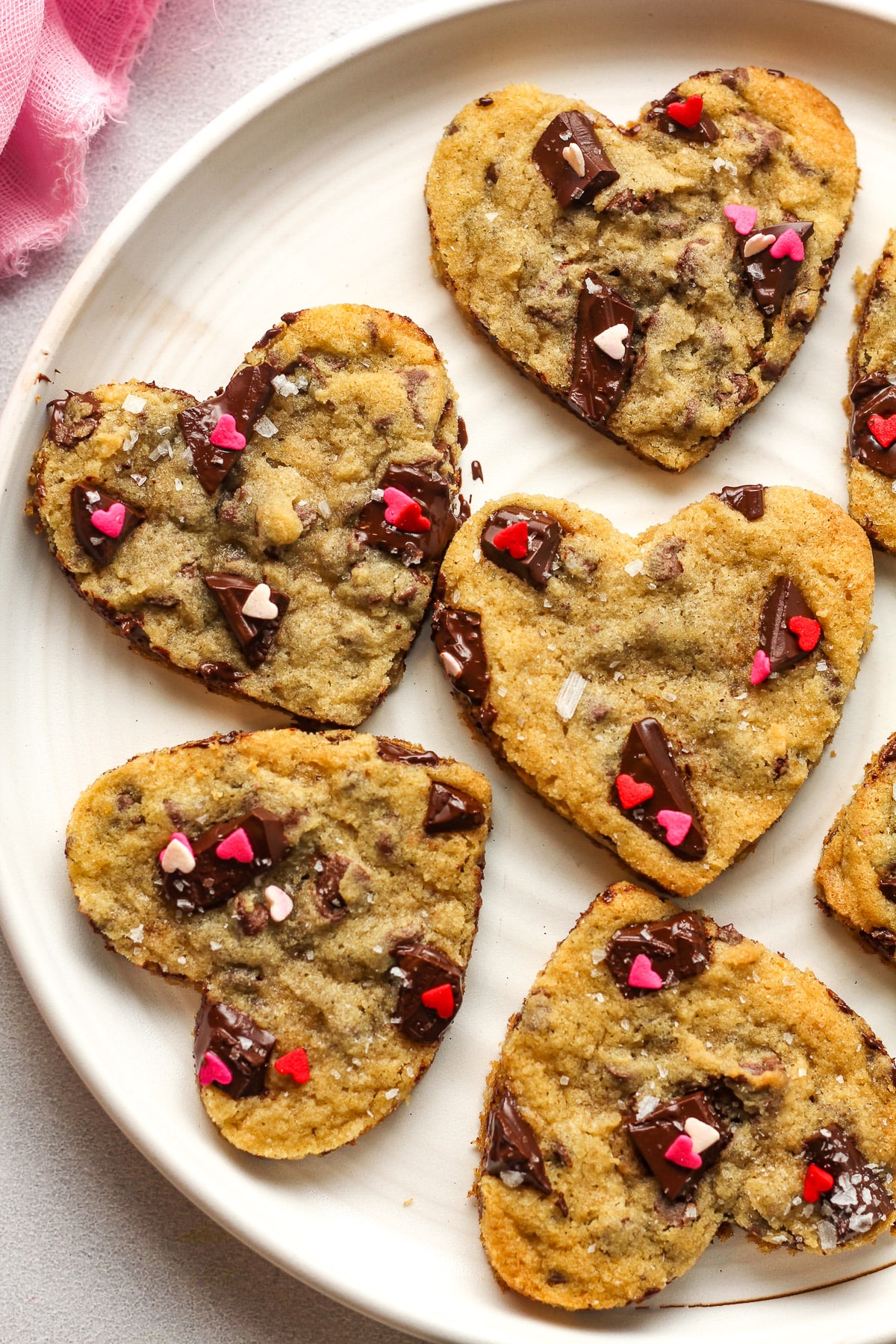 Overhead view of a plate of cookies cut into heart shapes with sprinkles.