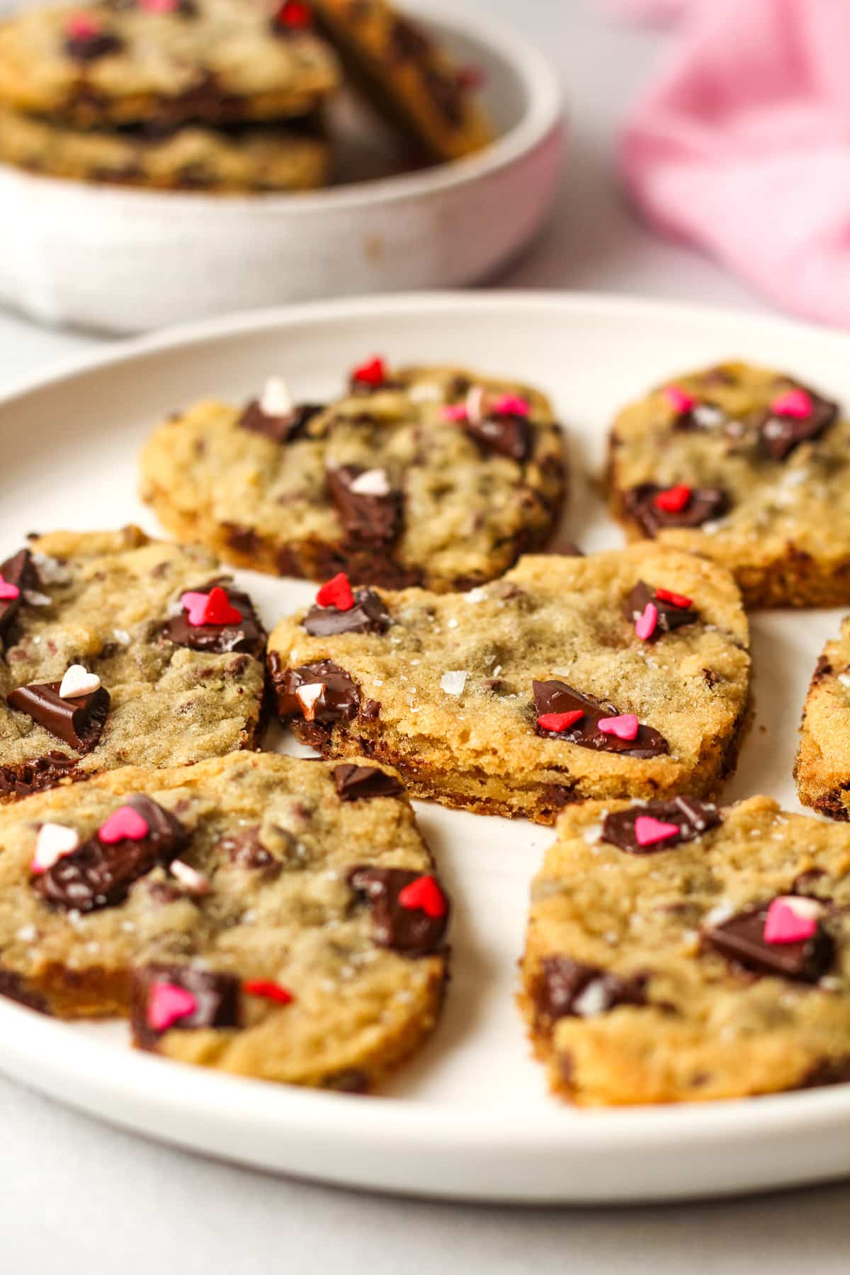 Side view of a plate of heart shaped chocolate chip cookies with sprinkles.