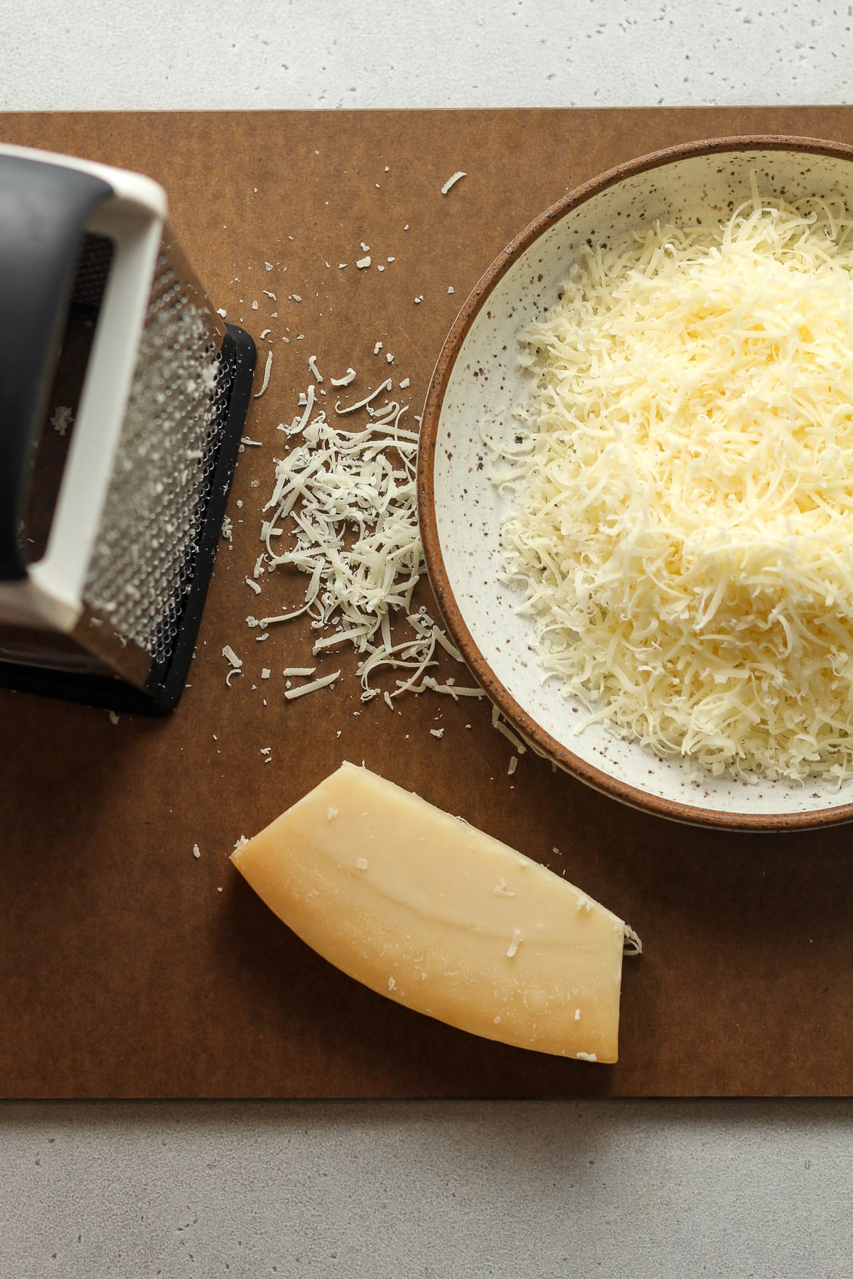 A board with a box shredder with a bowl of parmesan cheese.