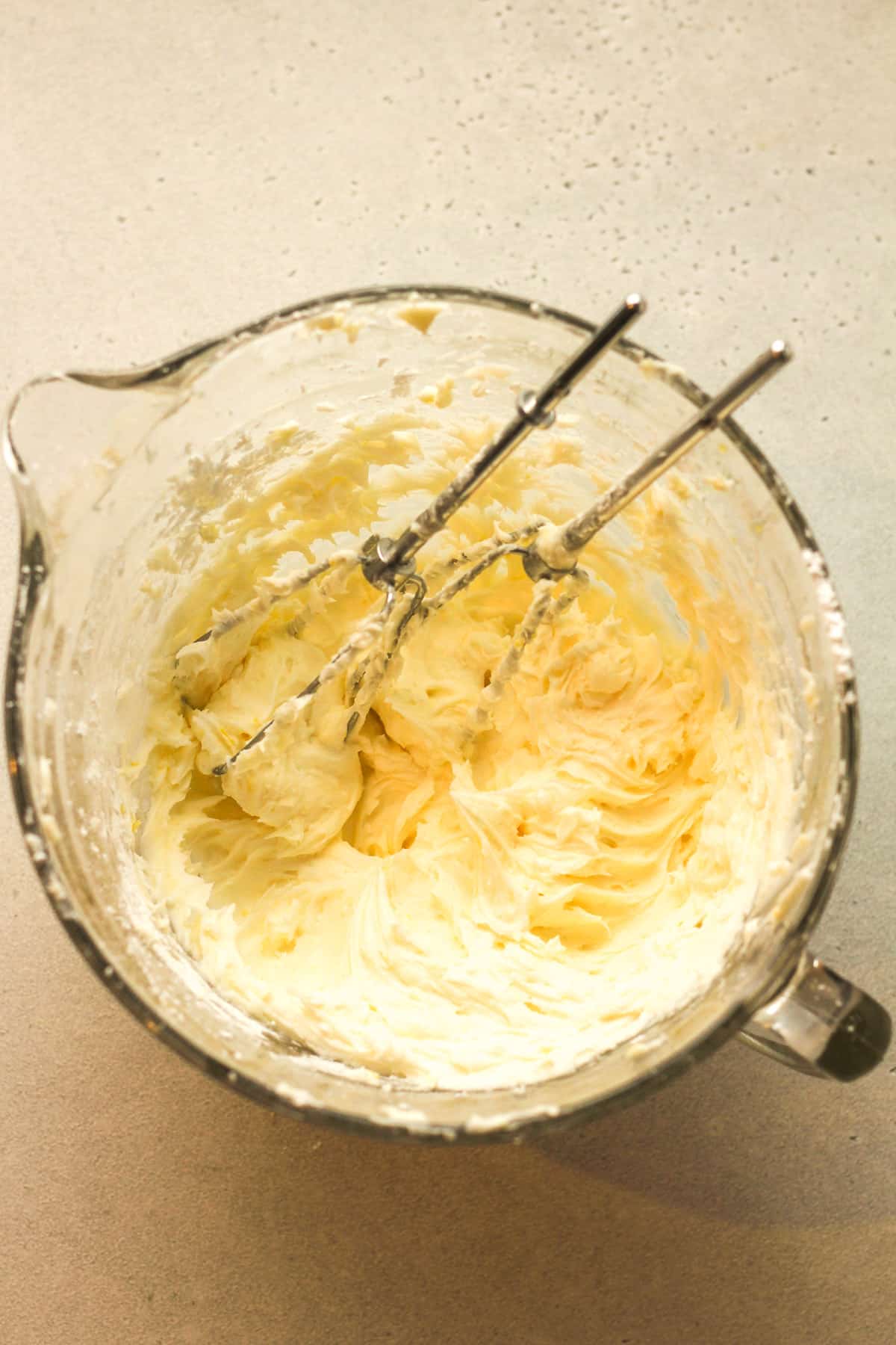 A large measuring cup of lemon buttercream with mixer attachments.