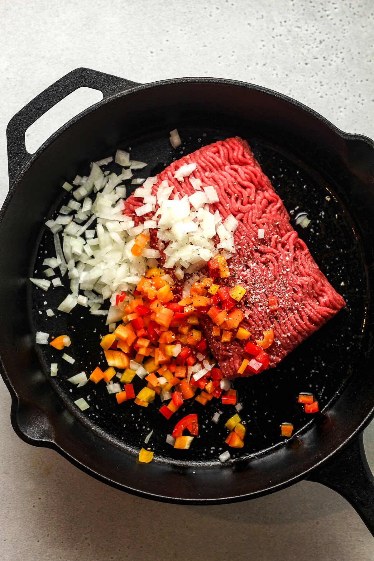 A skillet of the raw ground beef and diced onion and bell pepper.