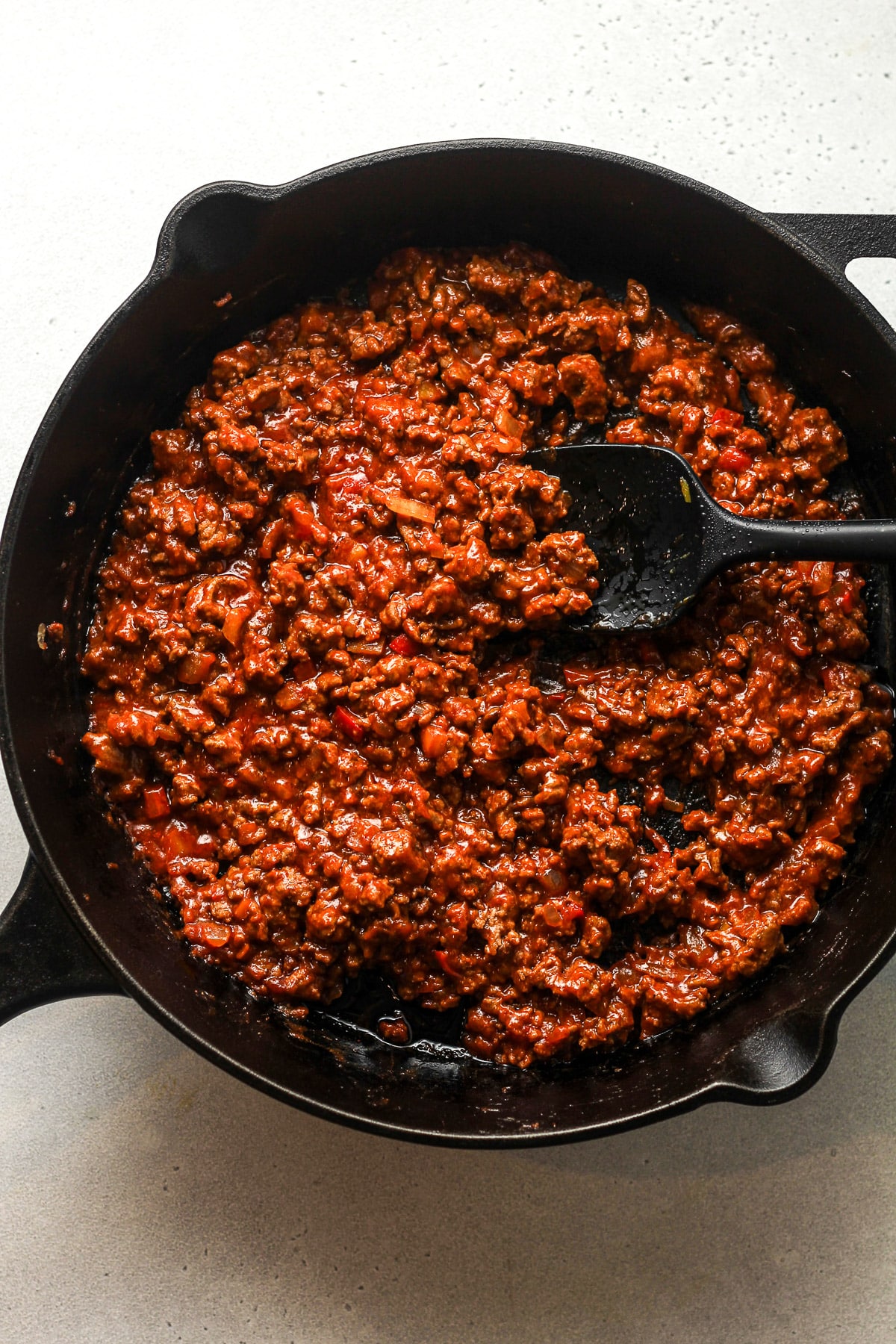 A skillet of spicy sloppy Joe mixture with a spatula.