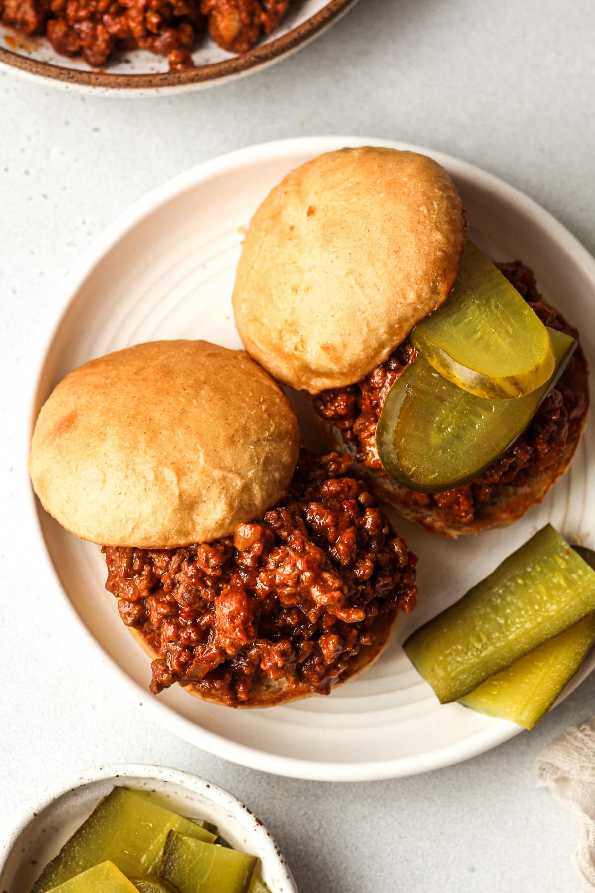 Overhead view of two toasted buns with sloppy joes mixture and pickles.