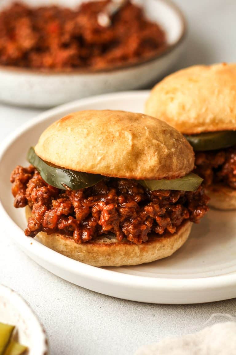 A plate of two sloppy Joe sandwiches with pickles.