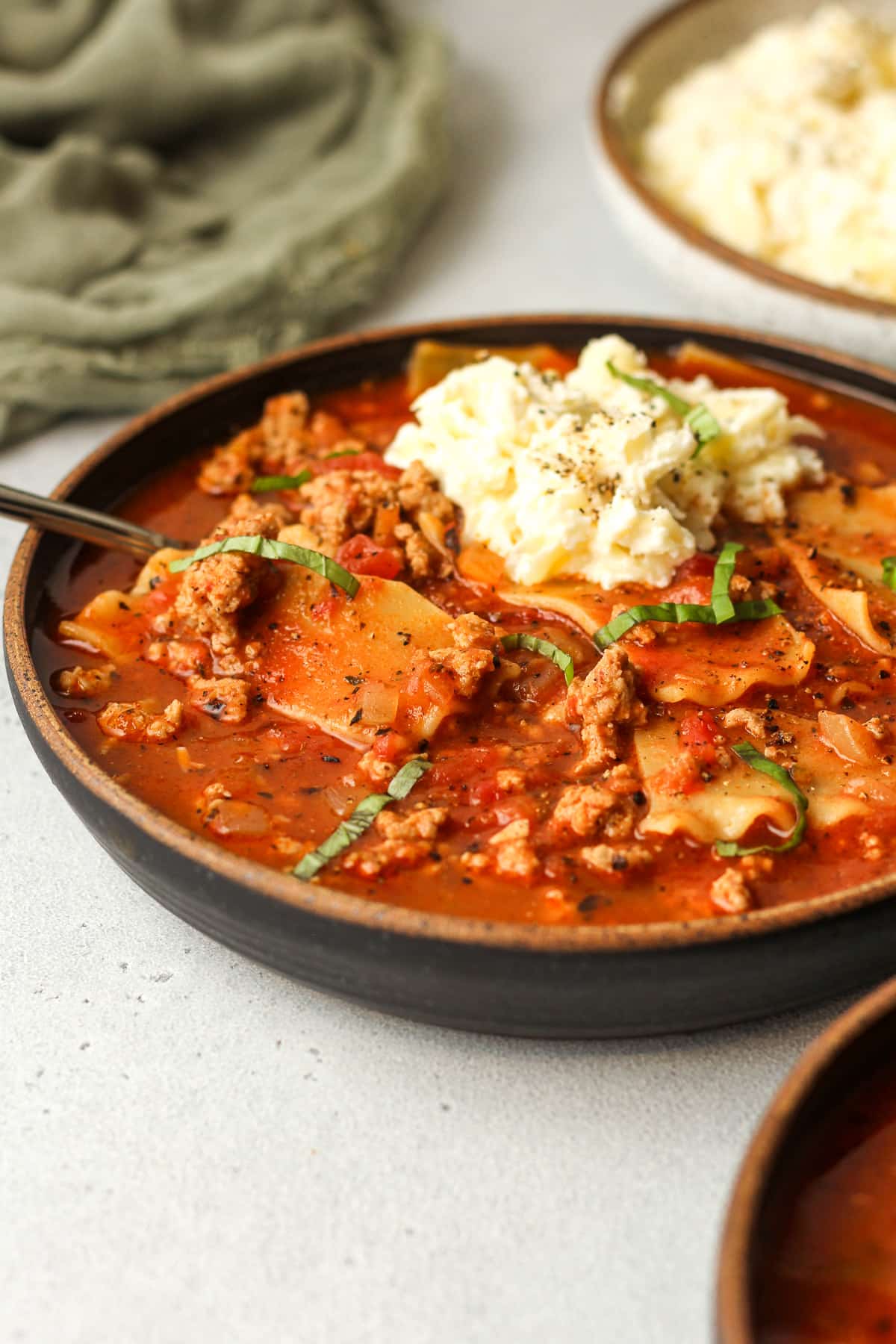 Side view of a bowl of lasagna soup with cheese and basil on top.