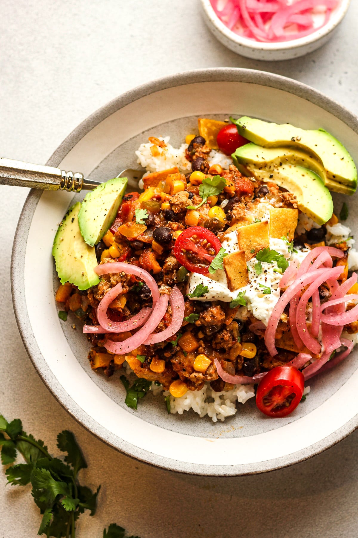 A bowl of rice topped with turkey taco skillet topped with sour cream, avocado slices, and pickled onions.