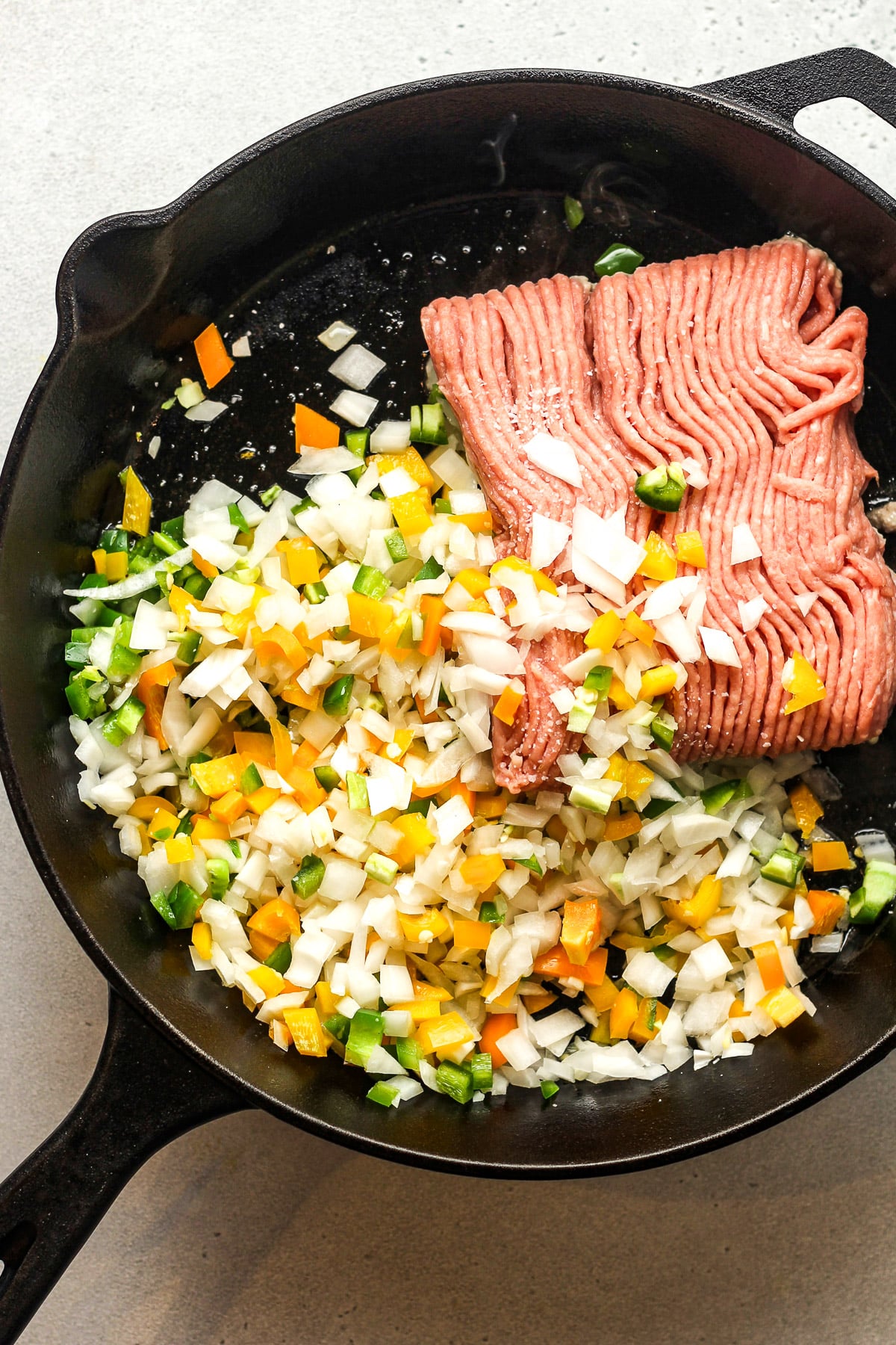 A skillet with raw ground turkey plus diced onions and peppers.