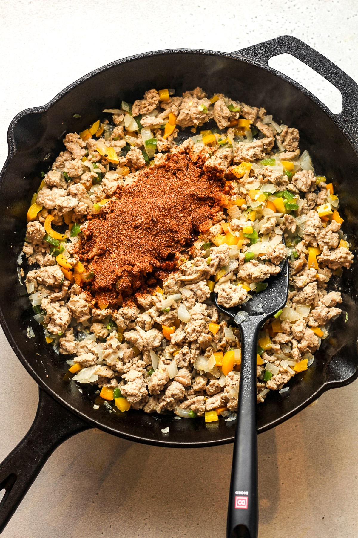 The skillet with browned turkey, veggies, and taco seasoning on top.