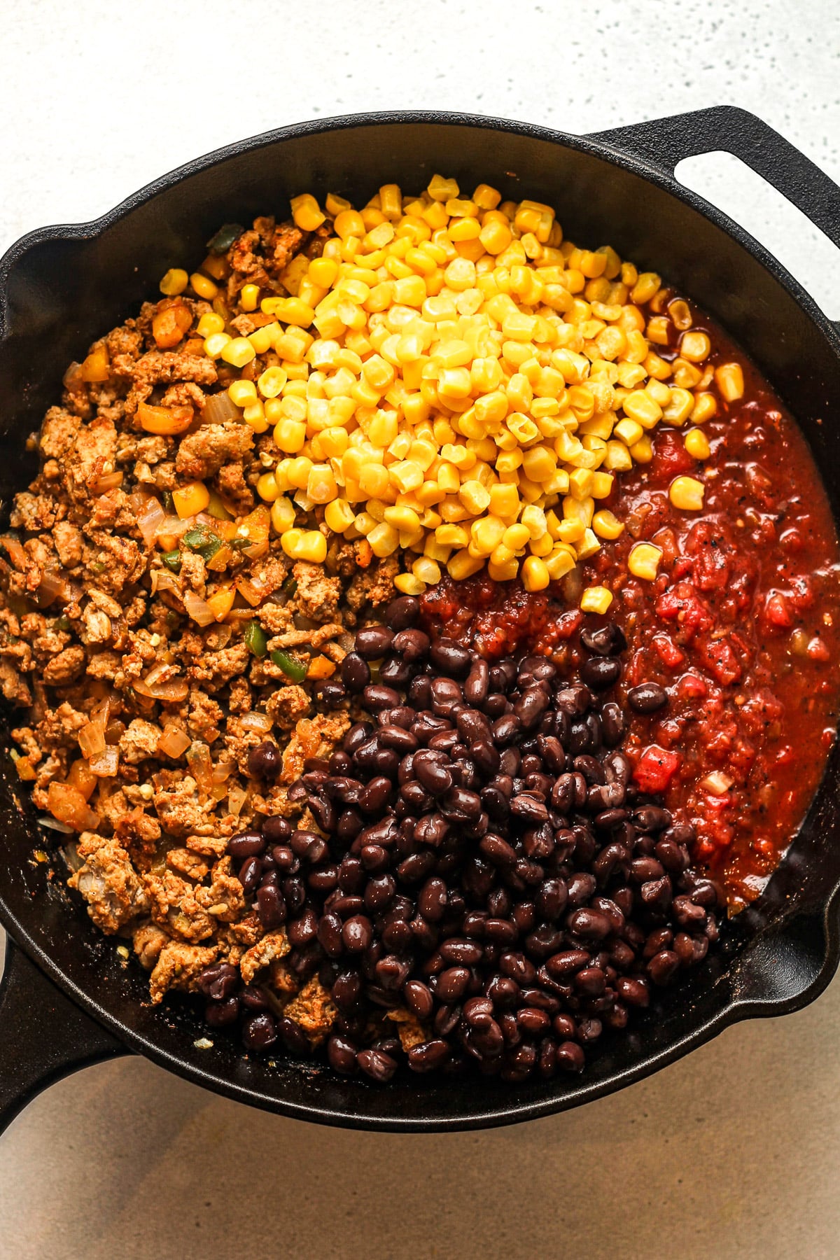 A large skillet with the browned turkey mixture plus black beans, frozen corn, and diced tomatoes before stirring to combine.