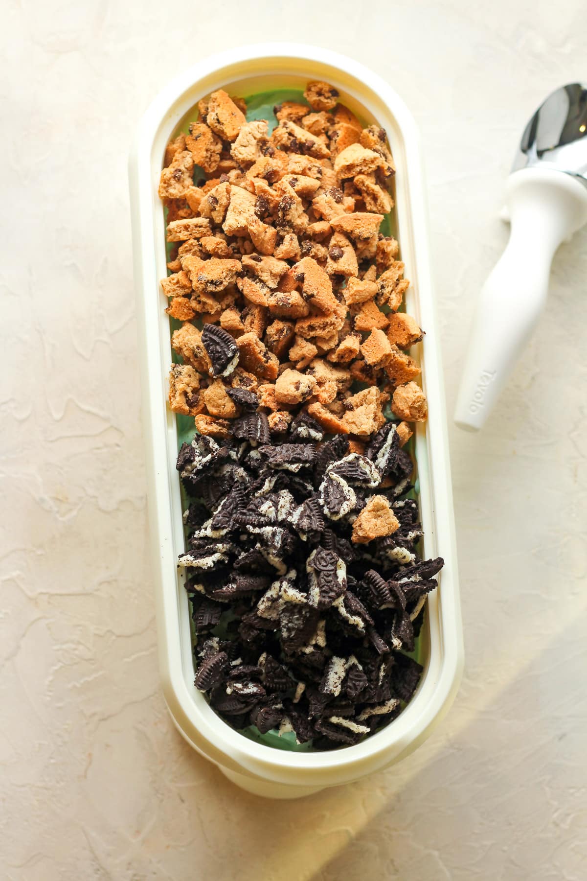 An oblong container of the ice cream base with the crumbled cookies on top.