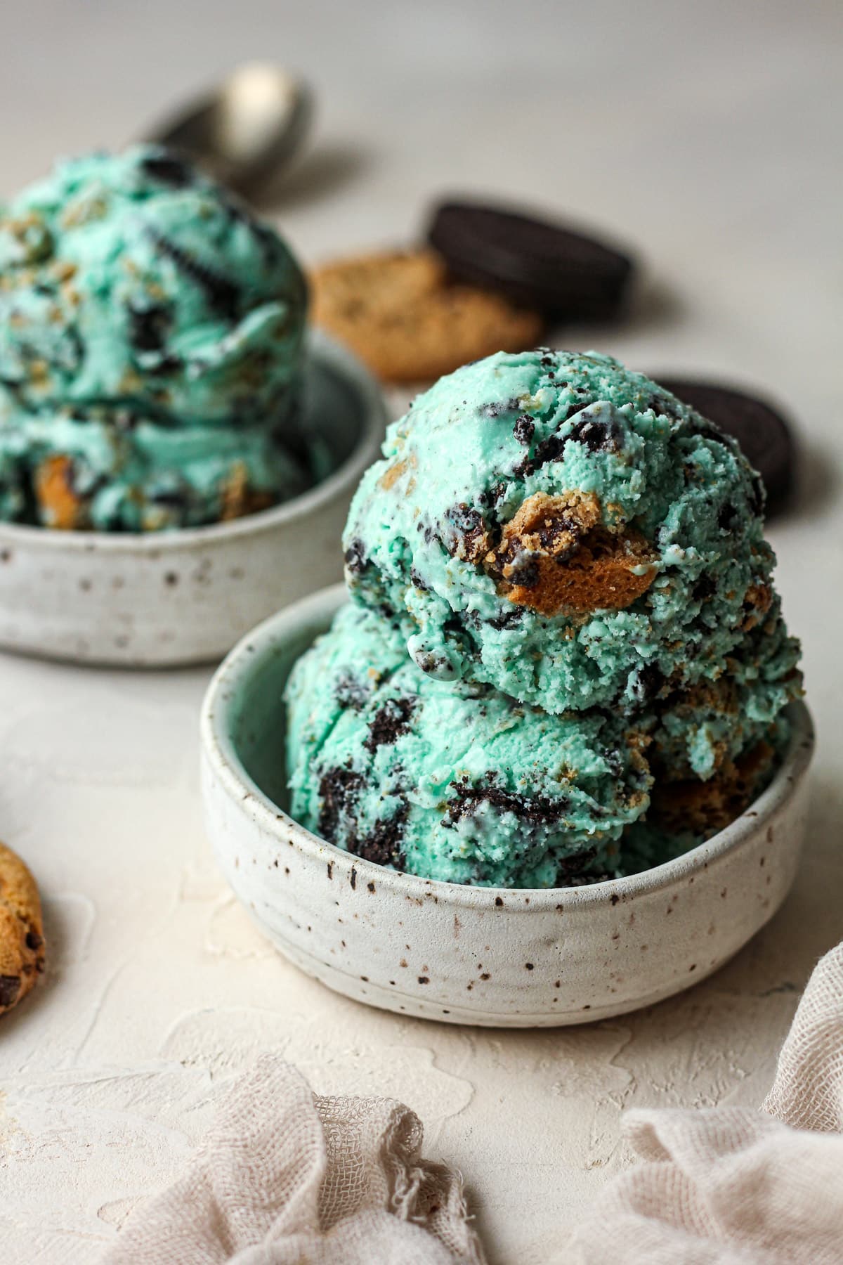 Side view of two small bowls of Cookie Monster ice cream with cookies in the background.