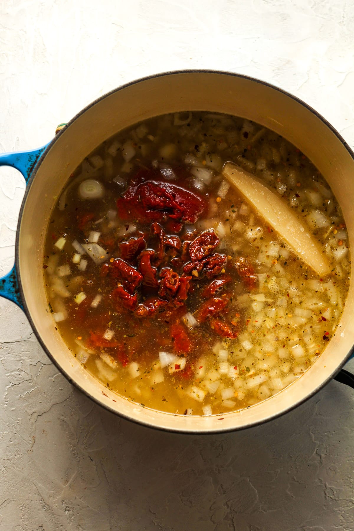 A stock pot of the sautéed onions plus tomato paste, sun-dried tomatoes, and parmesan rind.