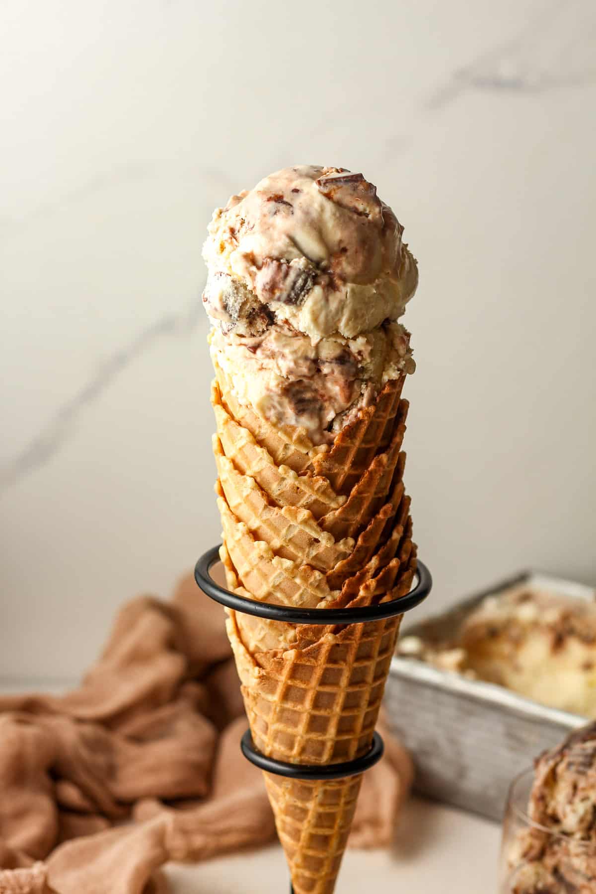 Side view of several stacked waffle cones with two scoops of moose tracks ice cream.