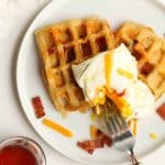 A plate of savory waffles with bacon, cheese, and an over easy egg.