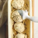 Overhead view of a container of four scoops of butter pecan ice cream with a scoop.