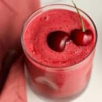 Overhead view of a cherry smoothie with fresh cherries on top.