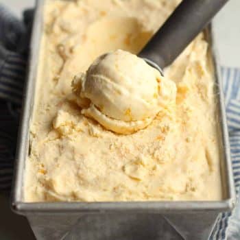 Side view of a scoop of homemade peach ice cream in a pan full.