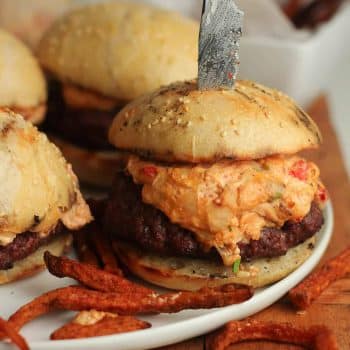 A plate with four pimento cheeseburgers with sweet potato fries.