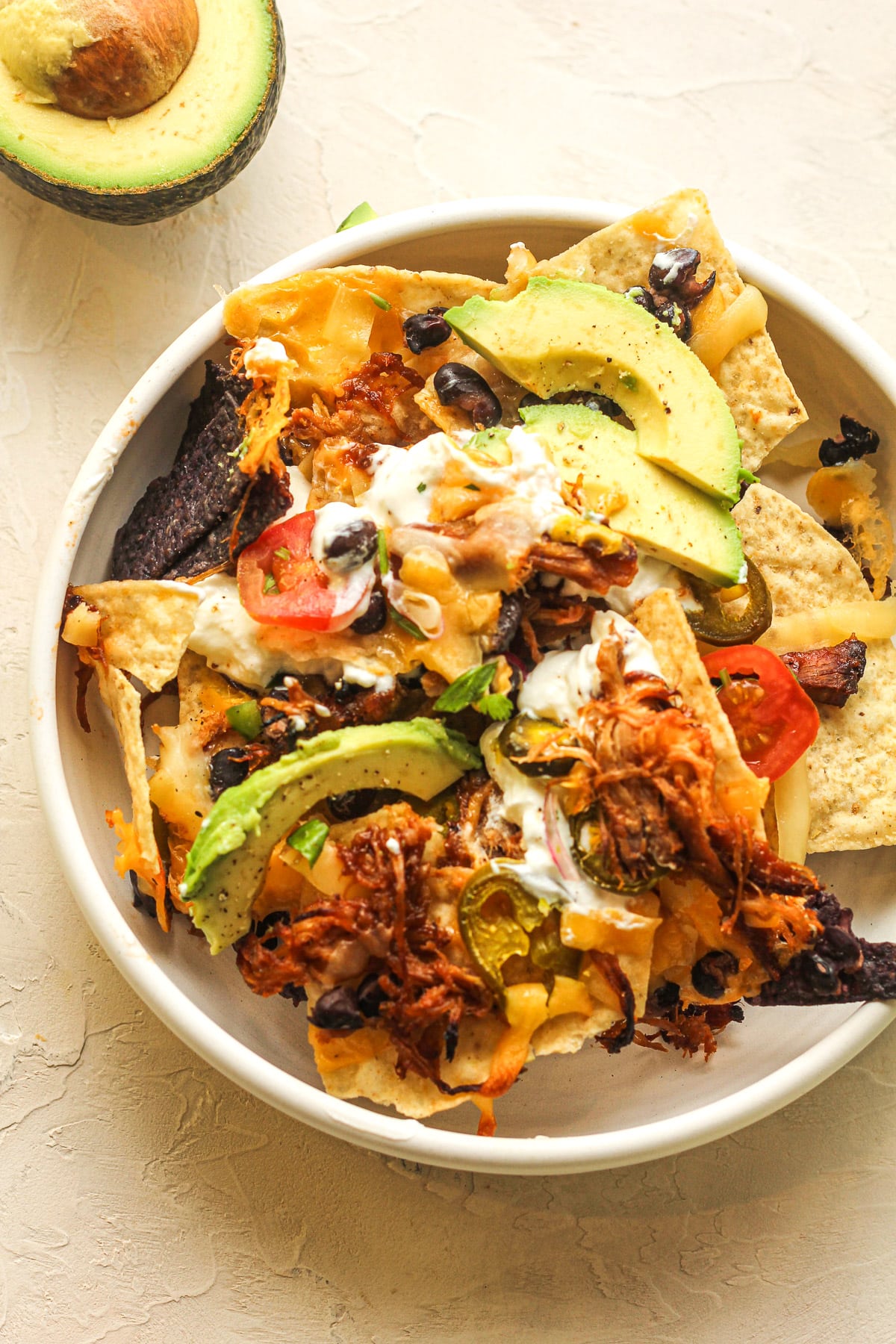 A bowl of a serving of pulled pork nachos with toppings.