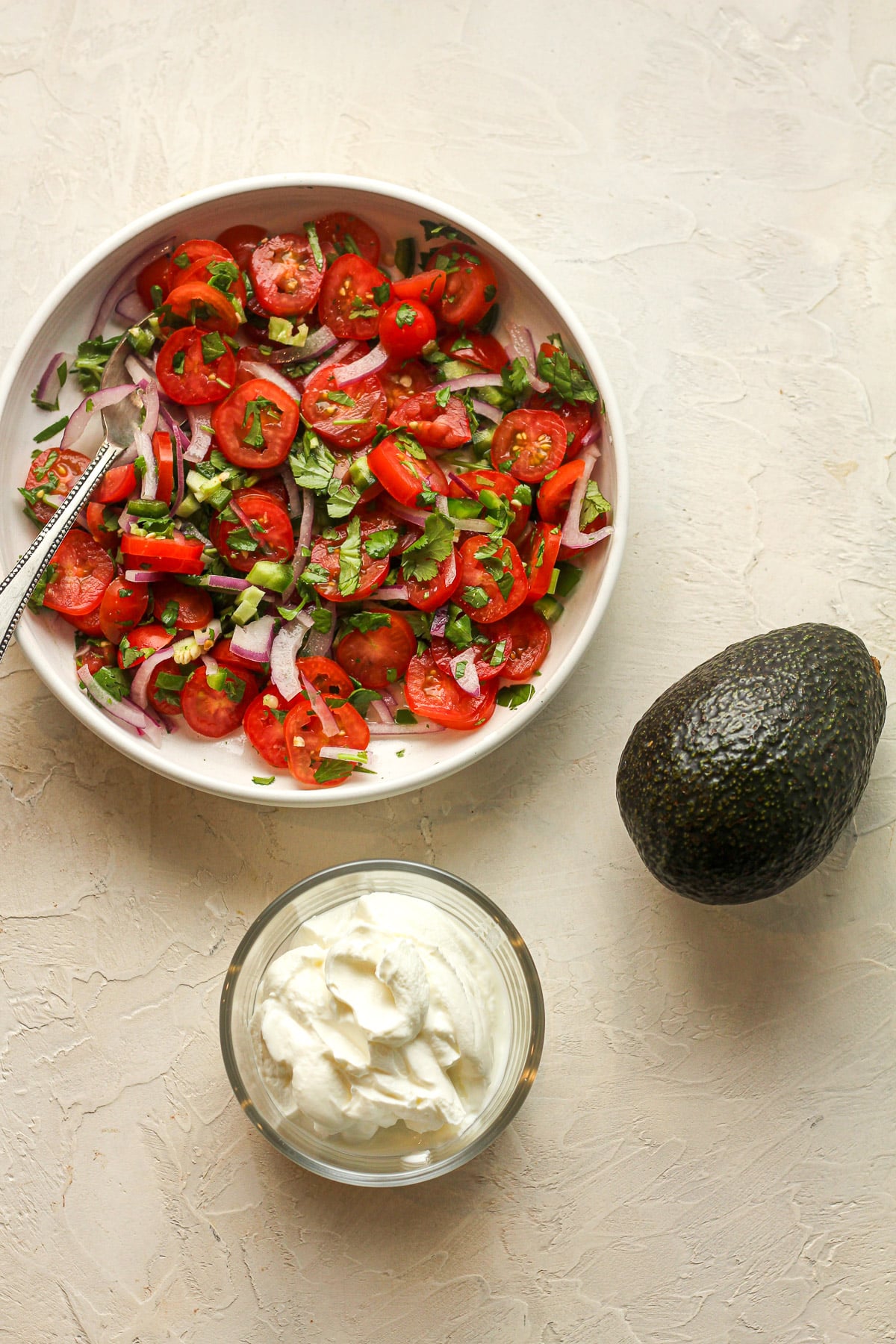 The toppings for the nachos - the pico de Gallo, sour cream, and a large avocado.