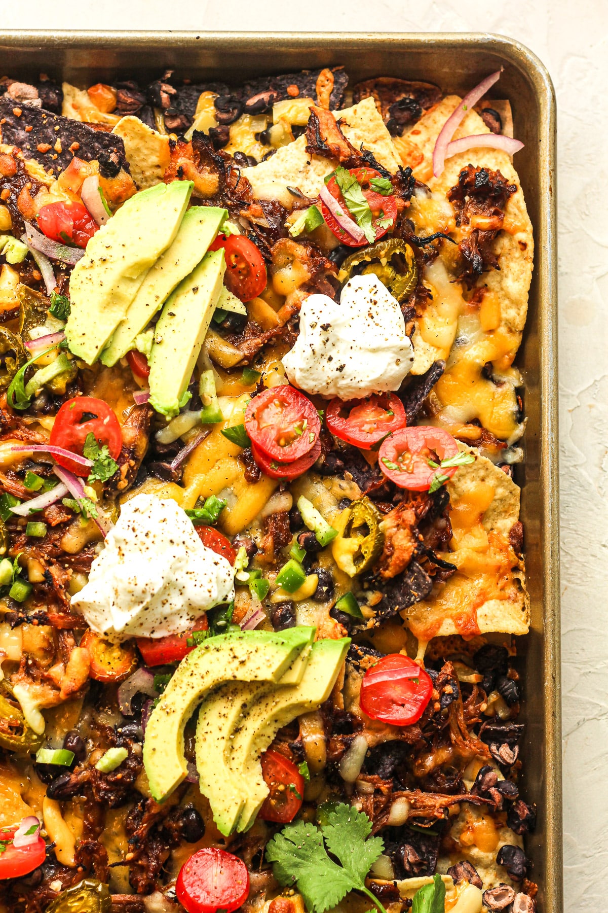 Overhead view of a pan of pulled pork nachos with pico de Gallo, sour cream, and avocado slices on top.