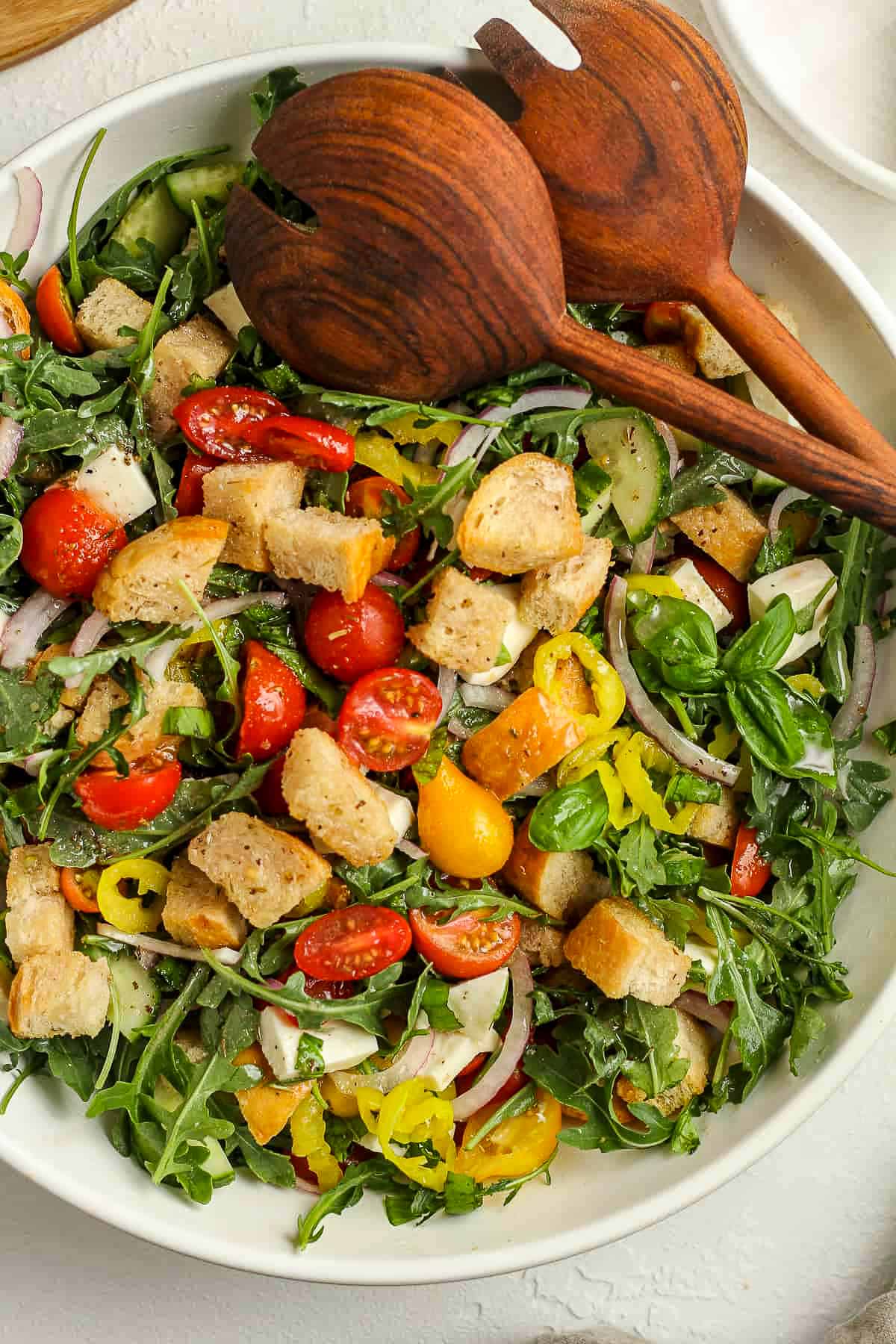 A large bowl of summer panzanella salad with wooden spoons.