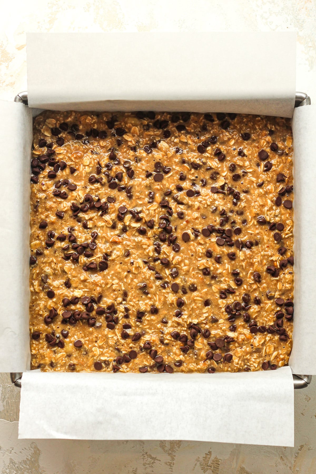The prepped oatmeal bars in a square pan with parchment paper.