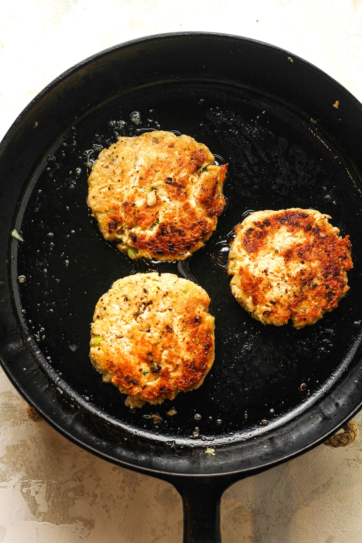 A cast iron skillet with three healthy tuna patties fried in oil.