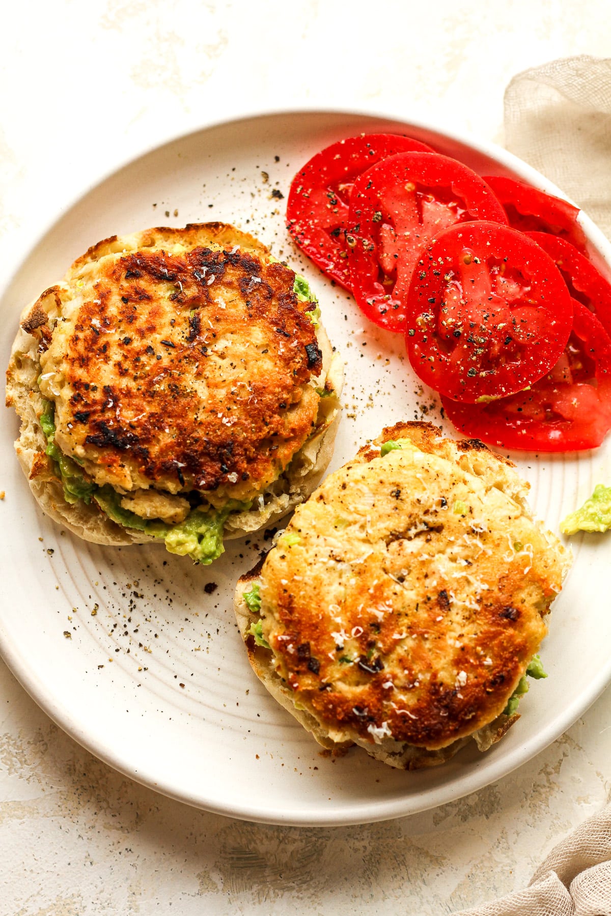 Overhead view of a plate of tuna patties on bread with mashed avocado and tomato slices.