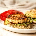 Side view of a plate of tuna patties on English muffins with avocado and tomato slices.