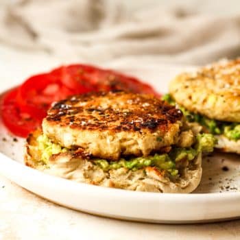 Side view of a plate of tuna patties on English muffins with avocado and tomato slices.
