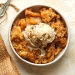 Closeup on a serving bowl of apple cobbler with a scoop of ice cream in the middle.