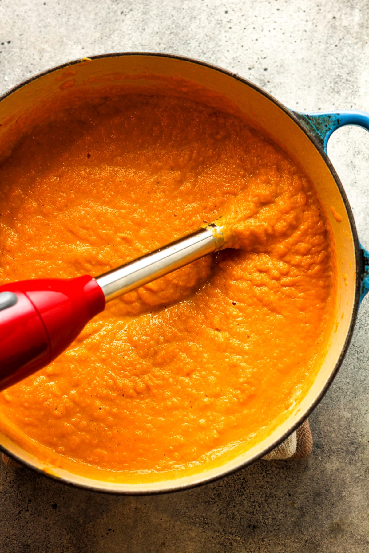 An immersion blender in the pot of squash soup after blending.