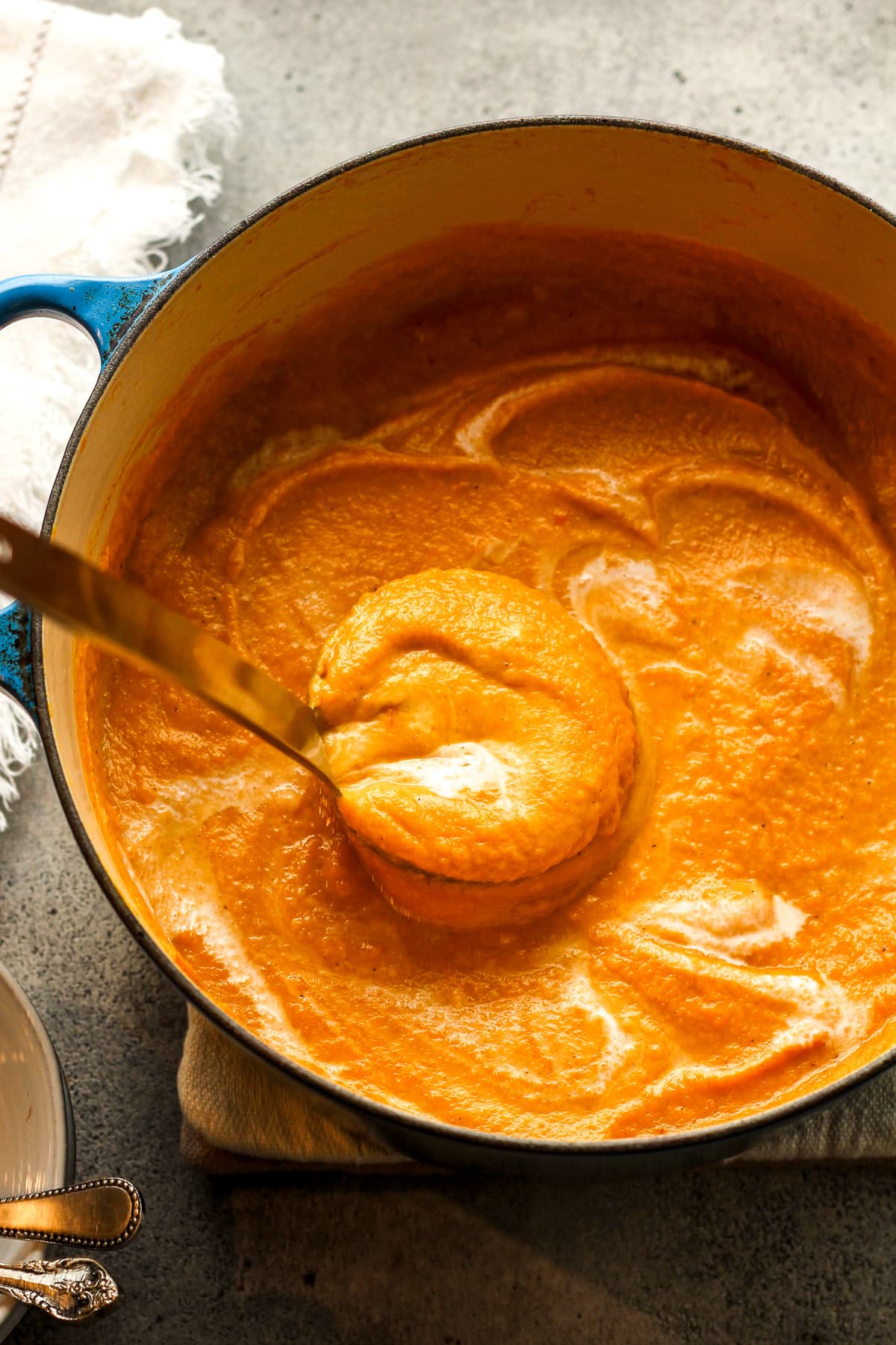 A soup ladle lifting up some Autumn squash soup out of the pot.