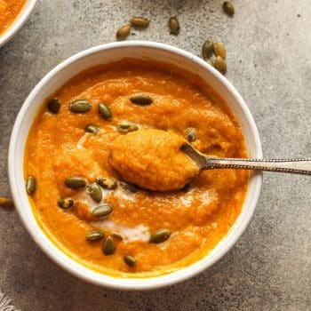 Closeup on a bowl of Autumn squash soup with a spoonful on top.